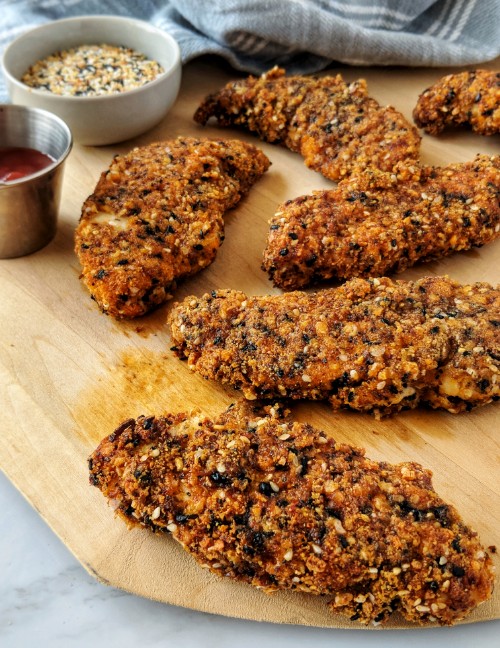 Chicken strips breaded in a mixture of grain-free ingredients are served on a wooden cutting board.